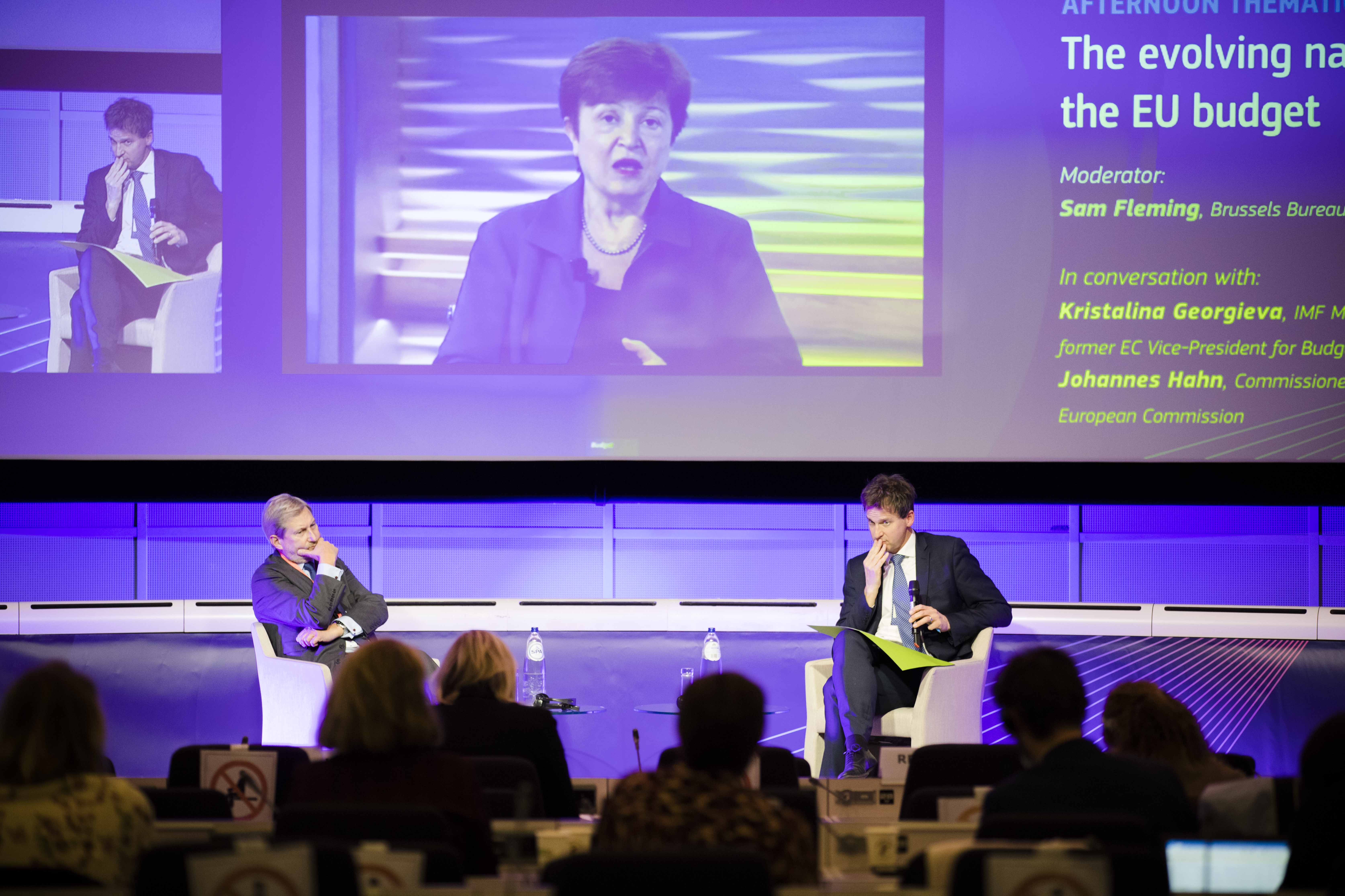 Kristalina Georgieva, Managing Director IMF on the screen speaking, below showing the satge  with Commissioner Johannes Hahn on the left and moderator Sam Fleming (Brussels Bureau Chief, Financial Times) on the right