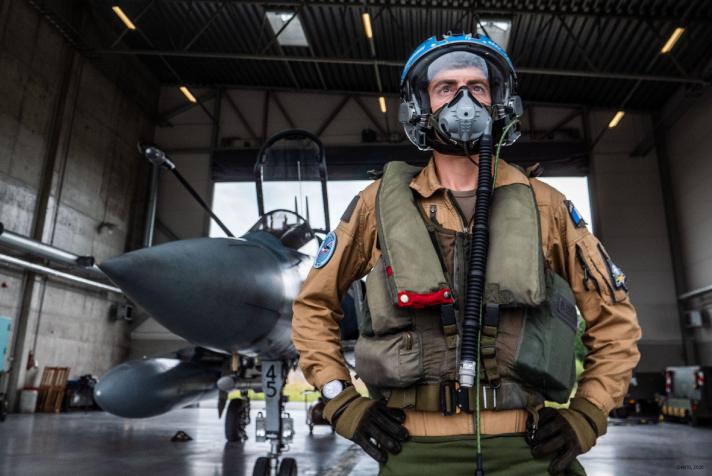A French fighter pilot standing in a hangar in front of a Mirage 2000 aircraft