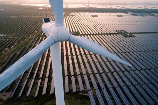 A wind turbine towering over a field of solar panels 