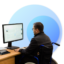man in a wheelchair in front of a desk, working on his computer 