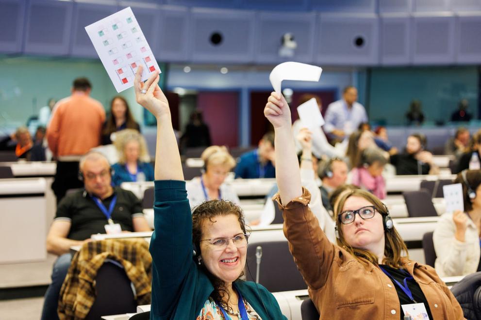 two ladies raise their arms and hold papers during a citizens panel session