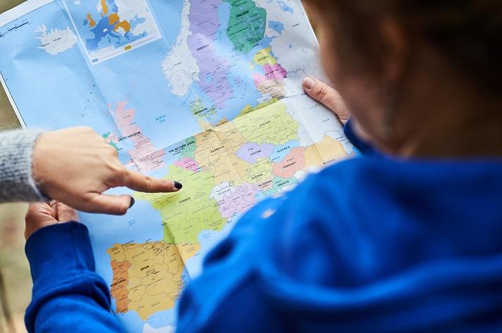 Women holding a map of Europe with someone pointing at the map