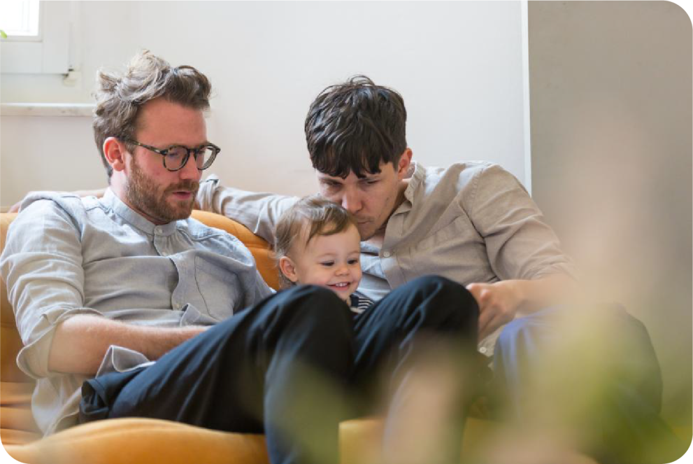 same-sex parents and their child sitting on a sofa at home