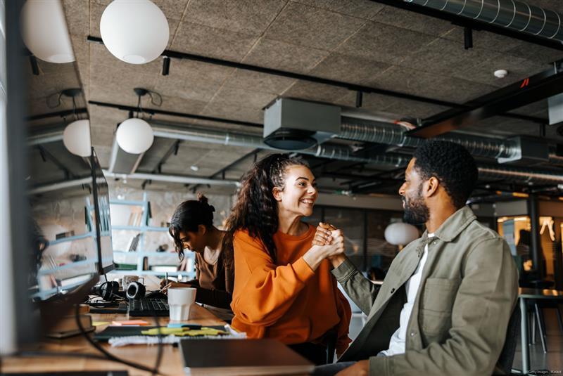 Excited male and female entrepreneurs celebrating achievement sitting at desk in office