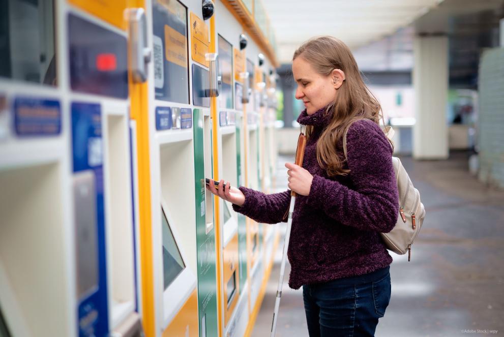 A woman with visual and hearing impairments buying a ticket at a ticket machine and paying by phone