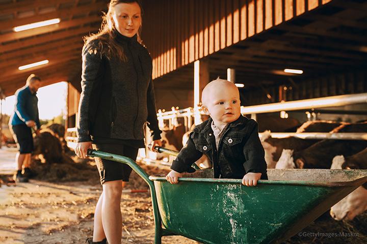 Young female farmer pushes a wheelbarrow with a child in it