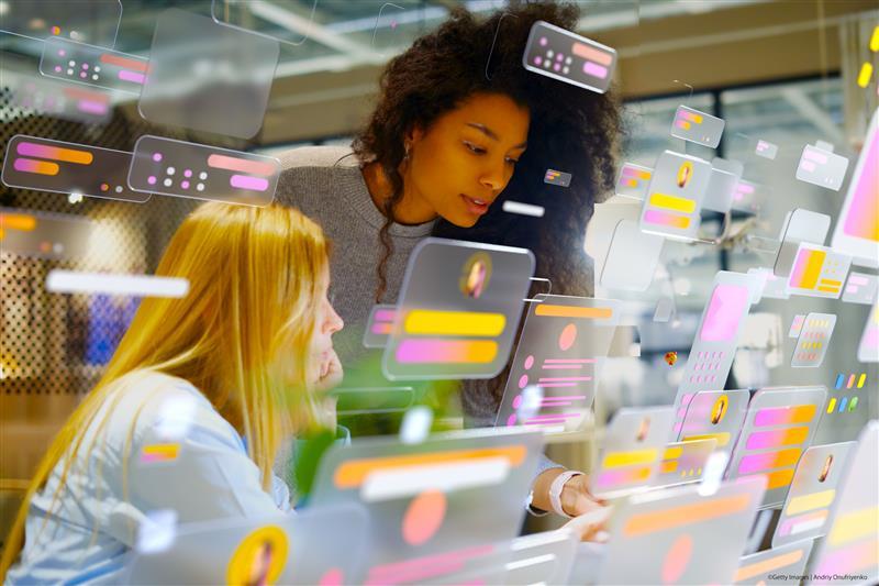Portraits of young women working in modern office surrounded by multicoloured social media icons and data screens. Data personalisation and social media concept