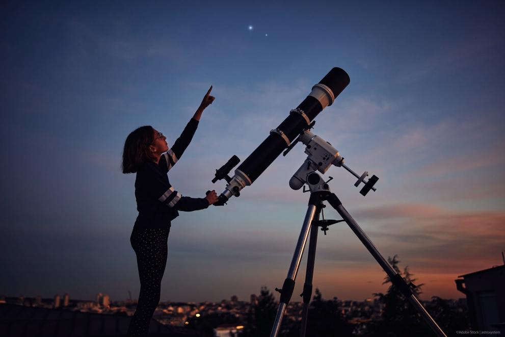 Girl with a telescope points at the night sky