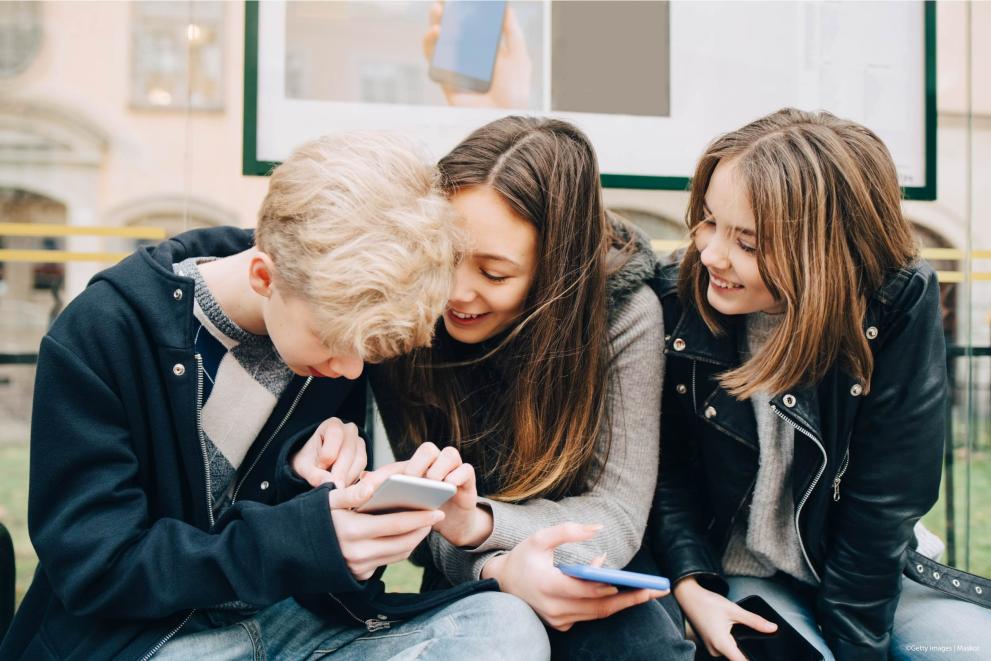Three kids holding smartphones and laughing