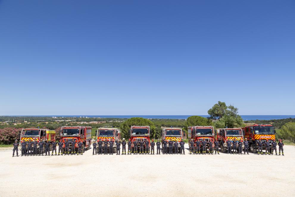 Romanian and French firefighters posing for a group photo in front of their fire trucks