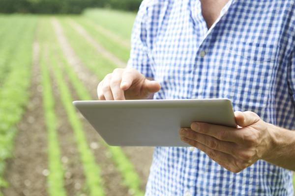man holding a tablet at a country field