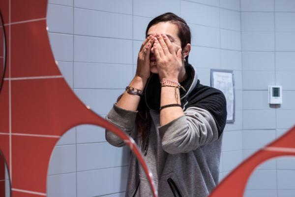 A distressed woman covering her face in a public restroom.
