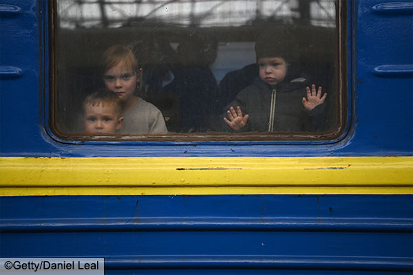 Children look out from a carriage window as a train prepares to depart from a station in Lviv