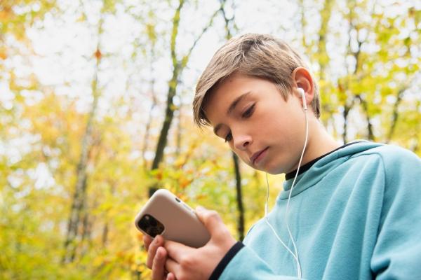 A child with a smartphone and earphones in the woods