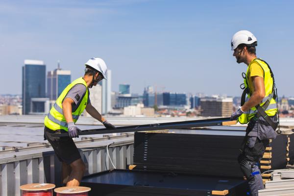 Two workers install solar panels on the roof of a building