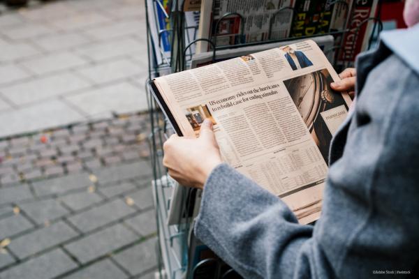 A person reading a newspaper at a newsstand.