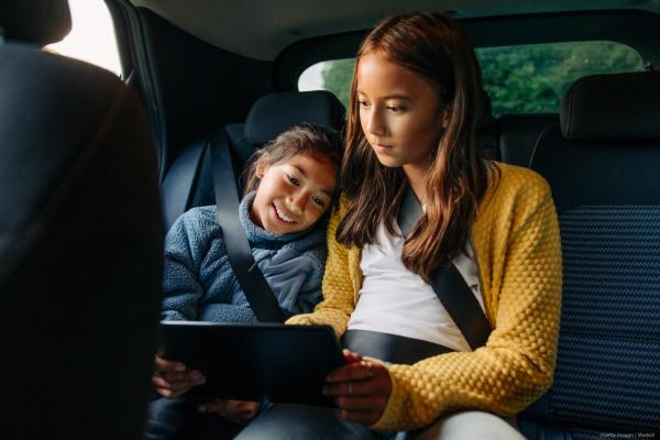 Sisters sharing tablet PC while sitting in car during road trip