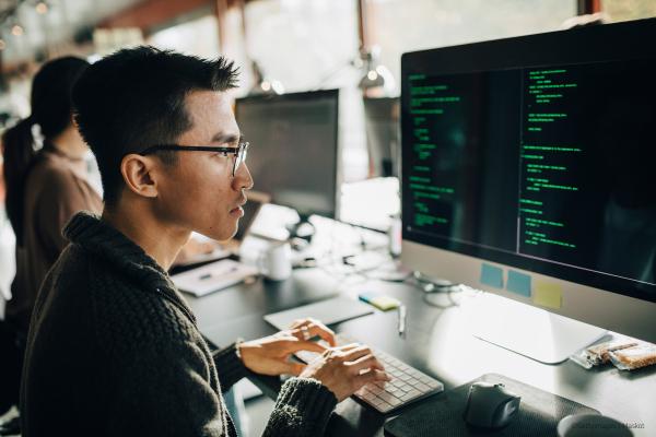 Side view of focused male developer coding on computer while sitting at working at office